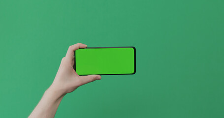 Young man hand hold smartphone with green screen on green background