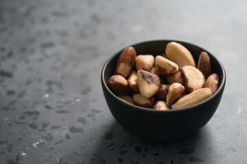 brazil nuts in black bowl on concrete background with copy space