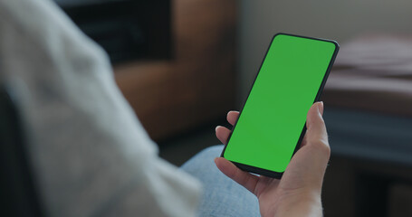 young woman sitting in a chair with smartphone with green screen