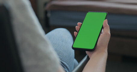 young woman sitting in a chair with smartphone with green screen