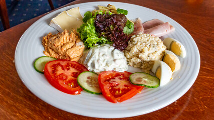 Dish with a combination of three different salads: Russian, tuna and shrimp accompanied by pasta, camembert cheese, human ham, egg pieces, lettuce with tomato and cucumber slices