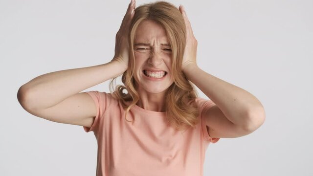 Annoyed blond girl covering ears with hands and does not want to hear anything over gray background. So loud expression