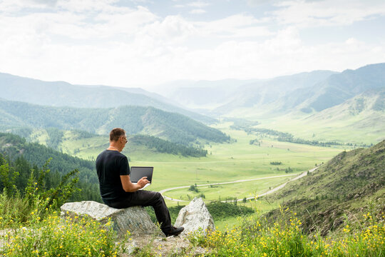  Traveler blogger work remote on netbook computer while enjoying mountain nature landscape view outdoors. man working outdoors with laptop.