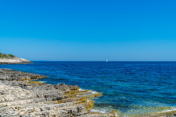 Rock beach with sailing boats in the background in Kamenjak National Park, Istria, Croatia