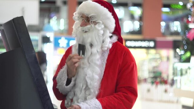 Santa Claus with a credit card near an bancomat in a large shopping center
