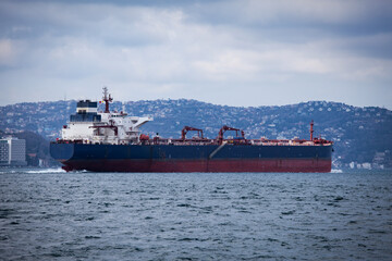 Fototapeta premium Huge tanker is passing through Istanbul strait or Bosporus. Giant cargo ship with couple of cranes over is sailing in Marmara sea on a cloudy day.