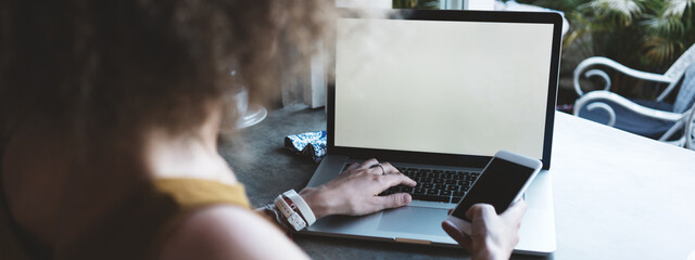 woman in city cafe, typing on mobile phone and laptop keyboard. Wide screen, panoramic