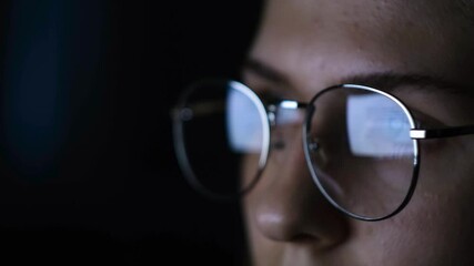 Close-up of woman with glasses looking at computer in dark. Concept. Woman with glasses straining eyes while reading articles on computer in dark