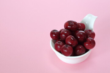 Fresh juicy cherries in white bowl on pink backgrond close up copy space
