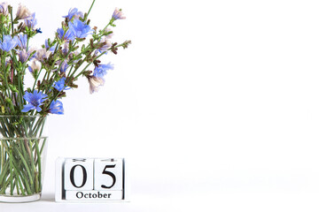 Flowers in a glass cup on a white background and a calendar with the date of October 5, a concept for the day of the teacher. Copy space.