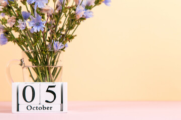 Flowers in a glass cup and calendar with date of October 5, on a colored yellow pink background, Teacher's Day concept. Copy space.
