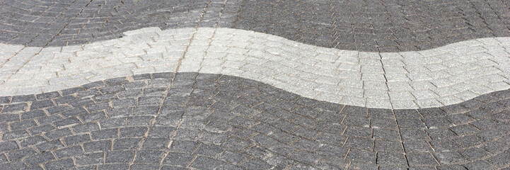 Wavy light and dark gray cobblestone pavement on the street. Panoramic image