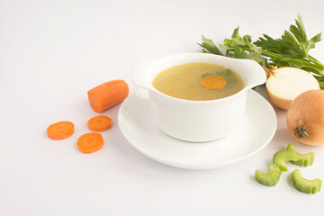 Chicken broth in the white bowl and vegetables on the light  background. Closeup.