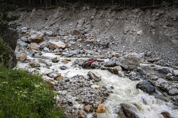 Red car broken and flushed by great mudslide. Rocky Adyl Su river in Caucasus. Kabardino-Balkaria, Russia.