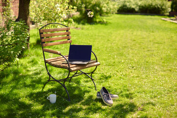 Obraz na płótnie Canvas A laptop with empty screen stands on a wooden bench in the courtyard, workspace of freelancer in beautiful home garden