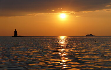 A distance silhouette of the lighthouse and a boat during sunset at Cape Henlopen State Park, Lewes, Delaware, U.S.A