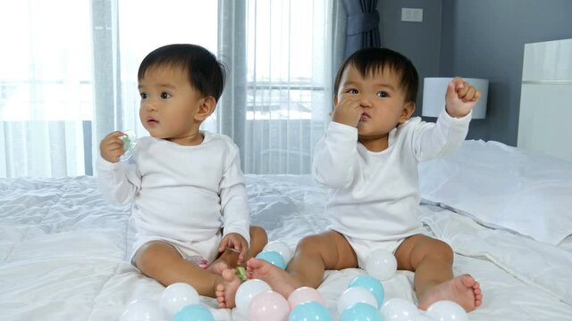 cheerful twin babies playing color ball on a bed
