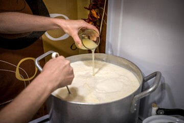 Unidentified woman is pouring ferment into hot milk during making traditional ossetian homemade cheese.