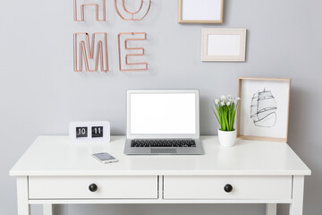 Modern laptop and mobile phone at workplace in room