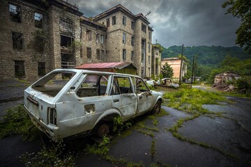Corrupted frame of old car near abandoned brick building in former Akarmara town, Abkhazia. Dramatic sky.