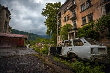 Corrupted frame of old car near abandoned brick building in former Akarmara town, Abkhazia. Dramatic sky.