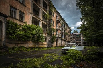 Corrupted frame of old car near abandoned brick building in former Akarmara town, Abkhazia. Dramatic sky.