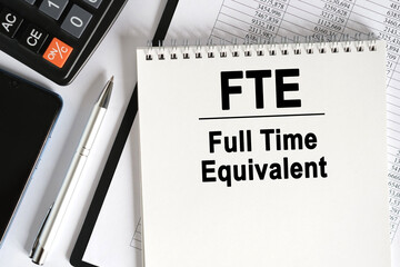 On the table lies a smartphone, a calculator and a notebook with the inscription- FTE.