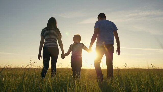 Happy family. Mom dad and son in an outdoor team walk through a green meadow at sunset. Healthy, active lifestyle of a married couple. Parents with a child have fun.