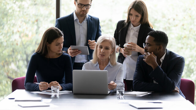 60s woman mentor teach young multi ethnic employees, group of diverse people analyzing online project offer business strategy, corporate team using computer app involved at brainstorm activity concept