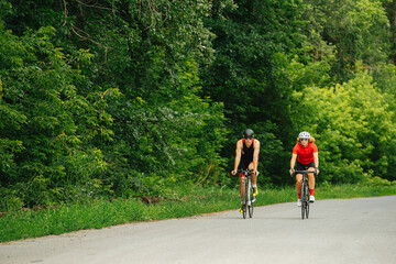 Сouple of professional cyclists biking on road through a forest on a summer day