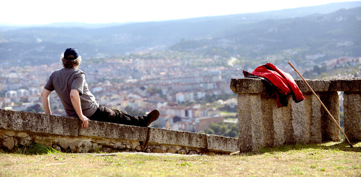 Senior man with backpack and hiking stick looks at a city from a hill