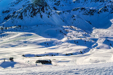 Panoramically view over mountains covered with snow and skiers in front of small hut in the valley...