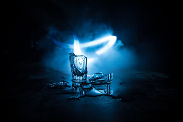 Broken glasses on wooden table at dark toned background with fog. Selective focus