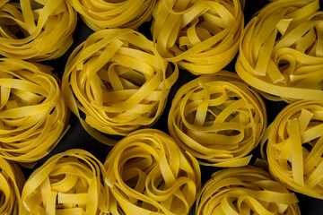 a lot of raw tagliatelle pasta on a dark background, top view.