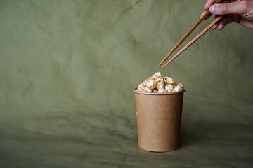 Chinese chopsticks to take popcorn from a box, a full can of popcorn, minimalistic style, on a colored background, concept picture, abstraction
