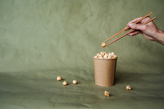 Chinese chopsticks to take popcorn from a box, a full can of popcorn, minimalistic style, on a colored background, concept picture, abstraction