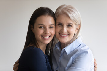 Head shot portrait blonde middle-aged mother and brunette millennial adult daughter embracing...
