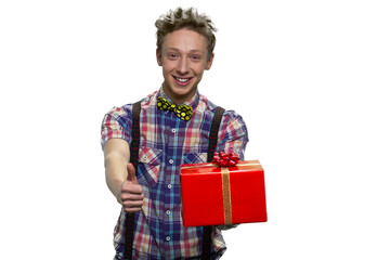 Smiling teenage boy's holding gift box and showing thumb up. Isolated on white background.
