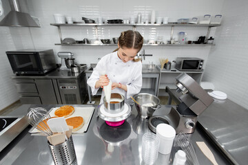 Confectioner apply cream from a pastry bag to the cake