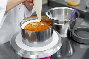 Confectioner apply cream from a pastry bag to the cake