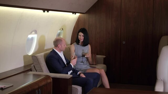 A young Business Couple Sitting on the Sofa In Their Business Jet, they Drink Champagne and Chat, Traveling Flying on a Private Plane