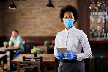 Portrait of African American waitress with protective mask in a cafe.