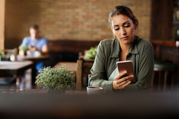 Young woman texting on mobile phone in a cafe.