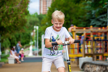 Little boy riding scooter in summer park