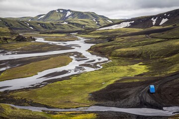 Highland in Iceland. Small winding rivers and streams are running between hills and mountains. Blue van is driving along the road.