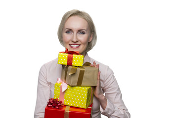 Pretty blonde woman in white blouse holding bunch of gift boxes on white background. Girl looking positively at camera with kind smile.
