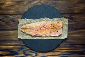 mackerel fillet on parchment and slate stand on a wooden table, top view