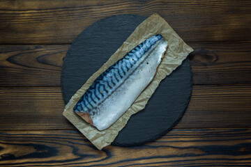 mackerel fillet on parchment and slate stand on a wooden table, top view