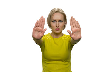 Young woman in yellow turtleneck making stop gesture with both hands on white background. No gesture or stop sign.