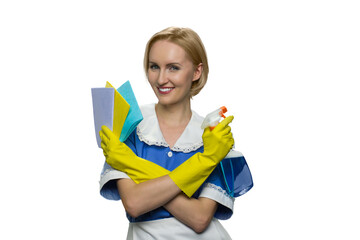 Young maid standing with arms crossed holding cleaning stuff on white background. Housekeeping cleaning service concept.